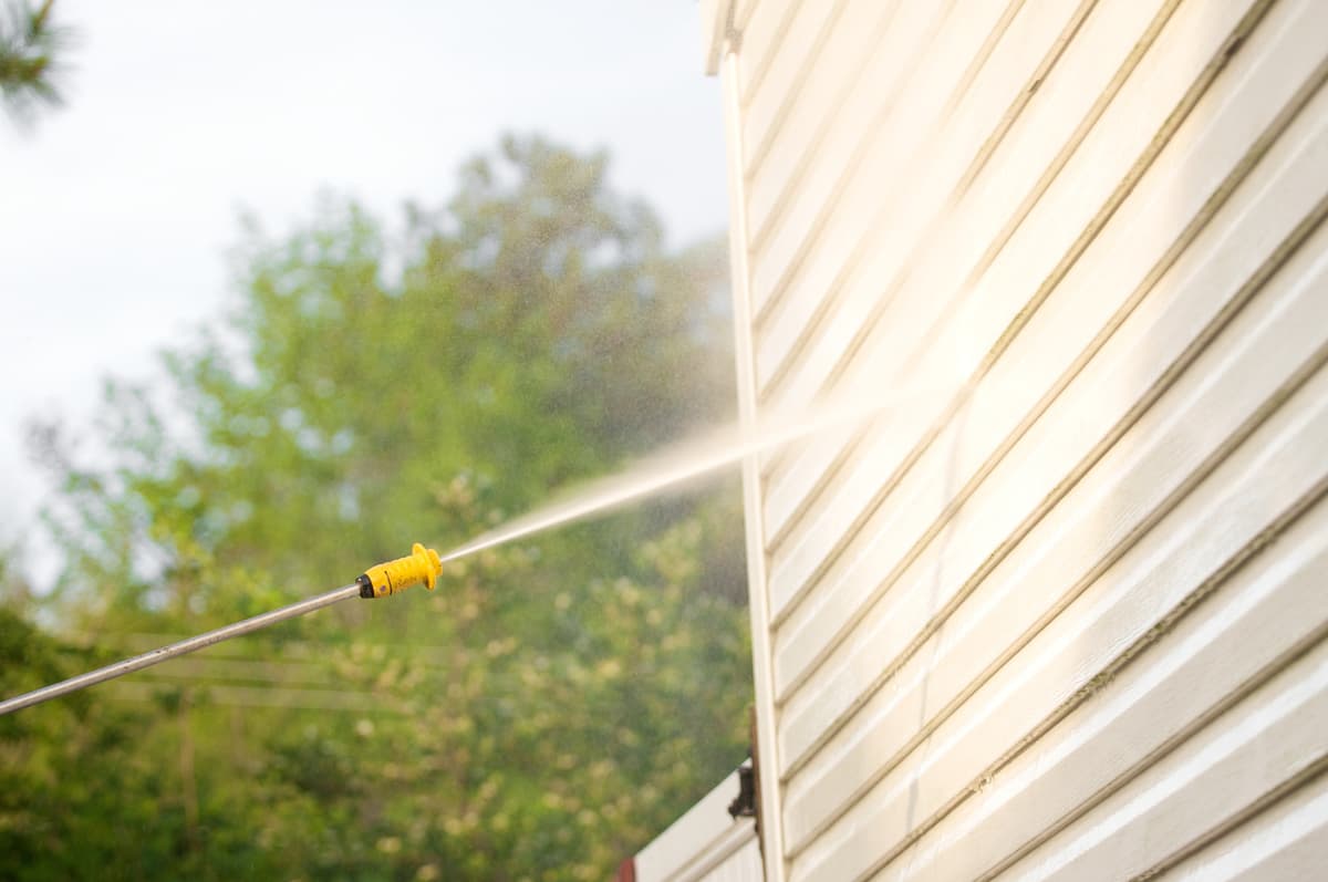 Pressure washer spraying cleaning solution on house siding